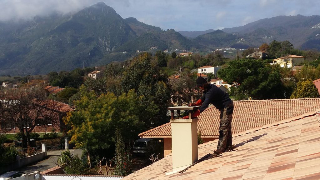 Ramoneur penché sur une souche de cheminée pour inspecter le conduit, montagnes en arrière-plan